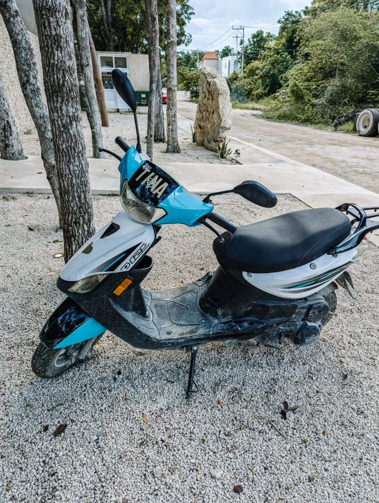 A parked blue and white scooter on a gravel path, ready for exploring during Chichen Itza day trips.